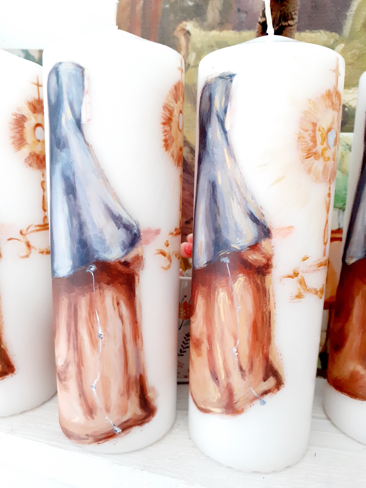 Ręcznie malowane, białe świece walcowe z wizerunkiem zakonnicy w brązowo-szarych barwach i motywem kwiatowym w odcieniach brązu i pomarańczy.