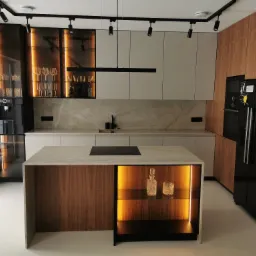 Nowoczesna kuchnia z wyspą, blatem z jasnego kamienia i oświetleniem LED podkreślającym szklane naczynia w barku.