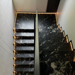 Kamieniarstwo Pietra Naturale - Nowoczesne schody z czarnego kamienia z podświetleniem LED, widok z góry. Minimalistyczna balustrada, eleganckie wykończenie.
