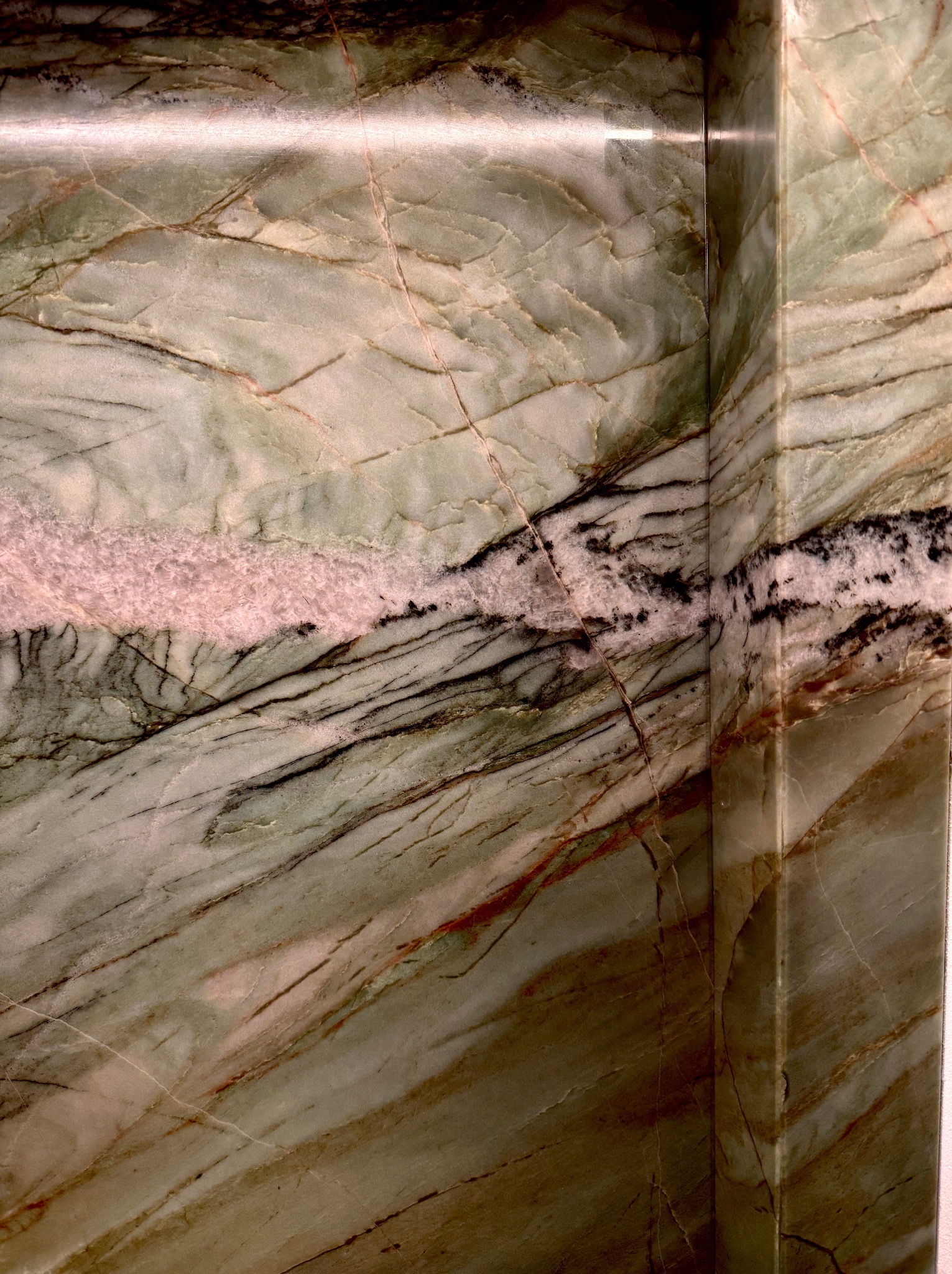 Fragment wykończenia wnętrza z zielonego marmuru z wyraźnym żyłkowaniem, ukazujący narożnik i gładką powierzchnię kamienia.