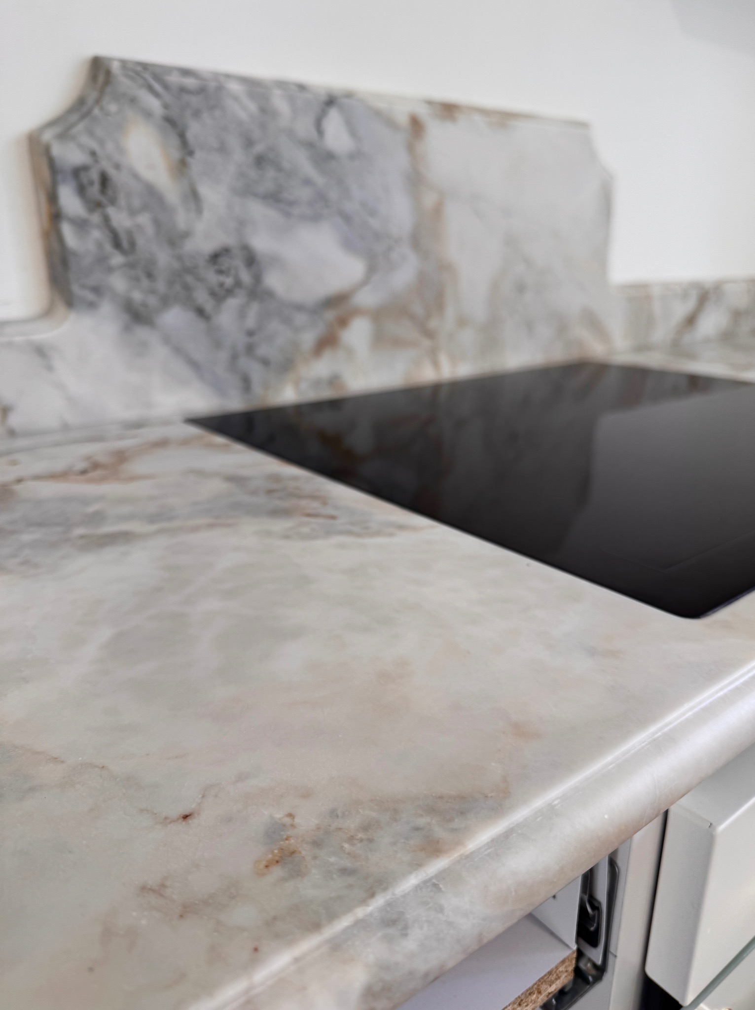 Jasny blat kuchenny z marmurowym wzorem, z wbudowaną płytą indukcyjną. Ujęcie z bliska, ukazujące detale wykończenia i strukturę kamienia.