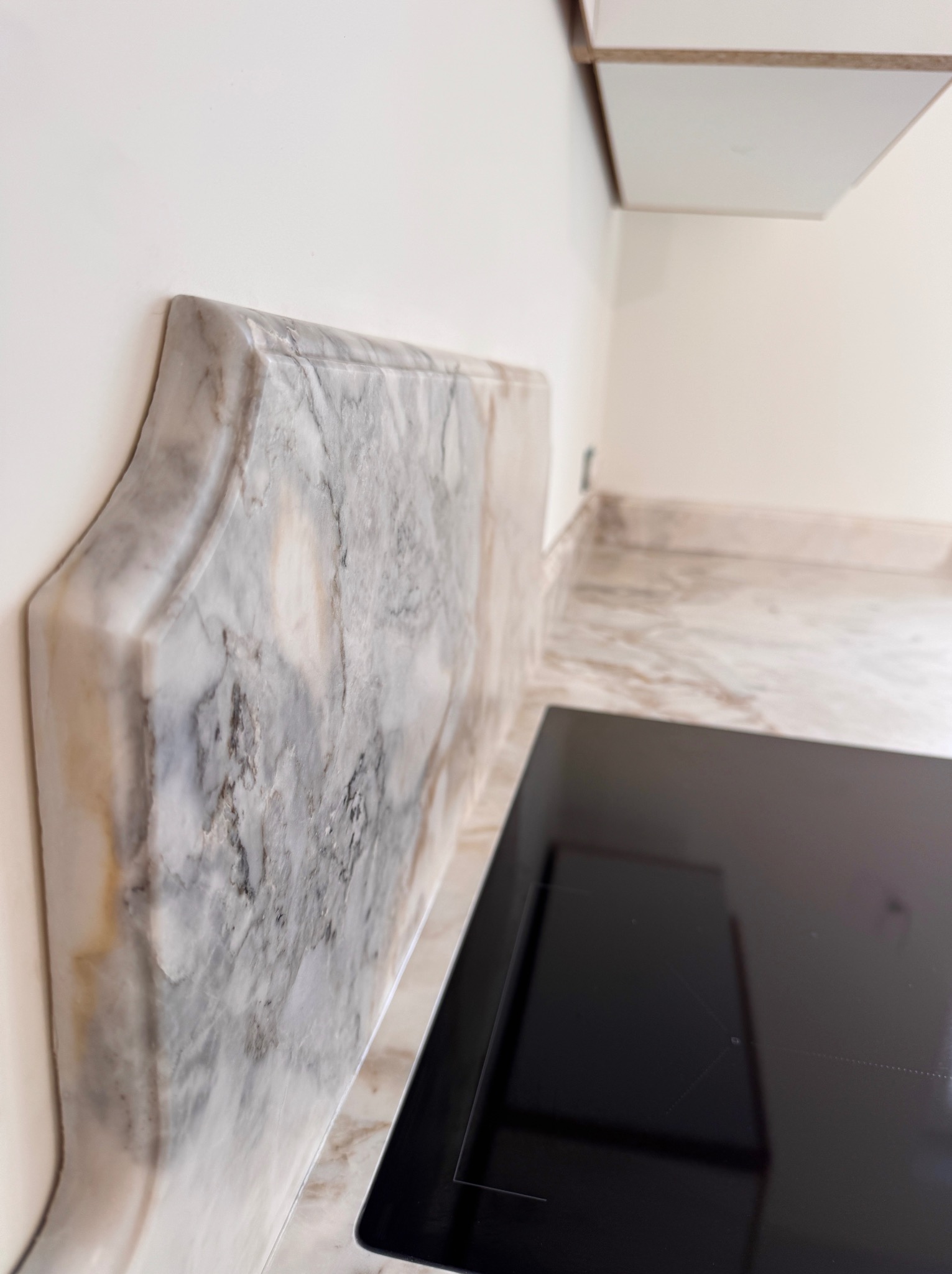 Marmurowy blat kuchenny z ozdobnym wykończeniem przy ścianie, obok płyta indukcyjna. Ujęcie z bliska, ukazujące detale kamienia i minimalistyczny design kuchni.