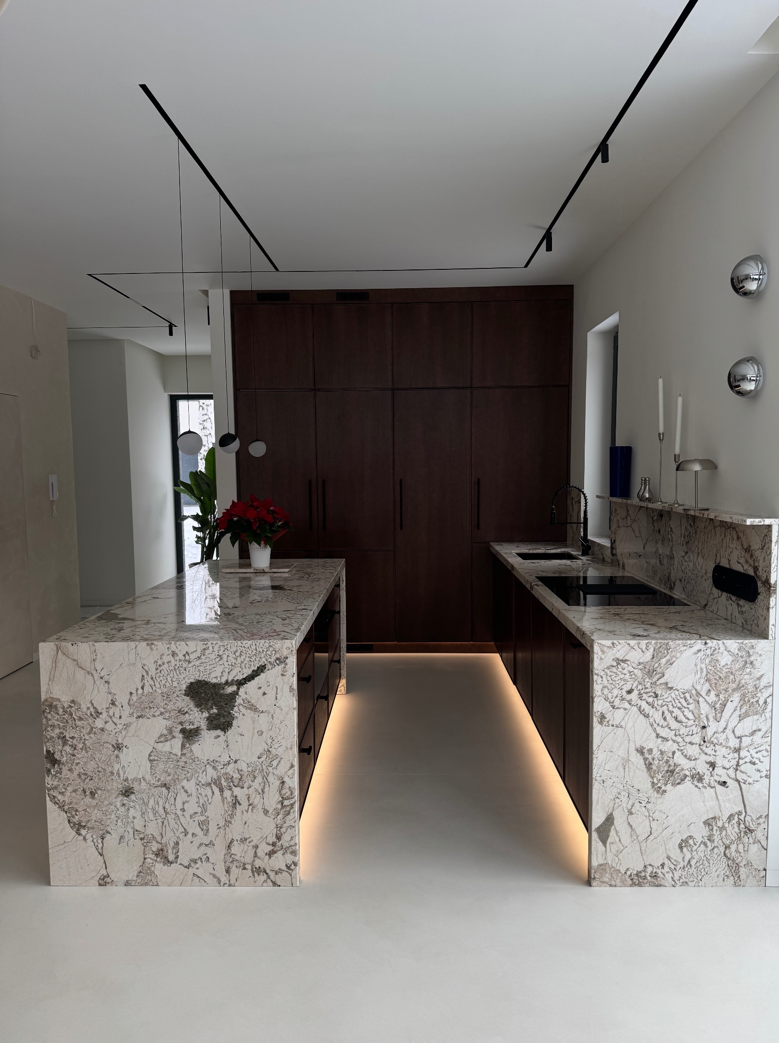 Nowoczesna kuchnia z wyspą i blatem z kamienia o unikalnym wzorze, podświetleniem LED i ciemnymi szafkami. Minimalistyczne oświetlenie sufitowe.