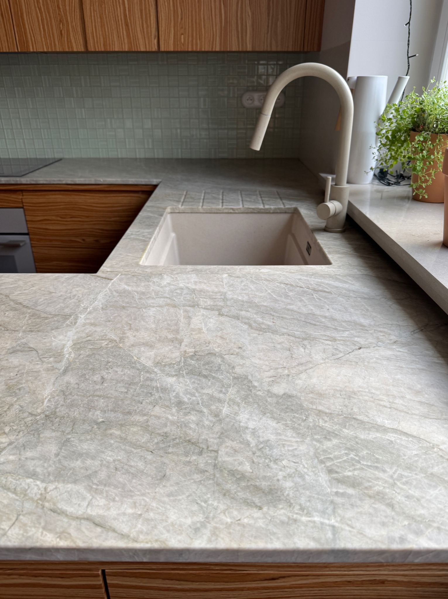 Jasnoszary blat kamienny z wbudowanym zlewozmywakiem, kremowa bateria, drewniane szafki i mozaika w tle. Widok z góry, podkreślający unikalny wzór kamienia.