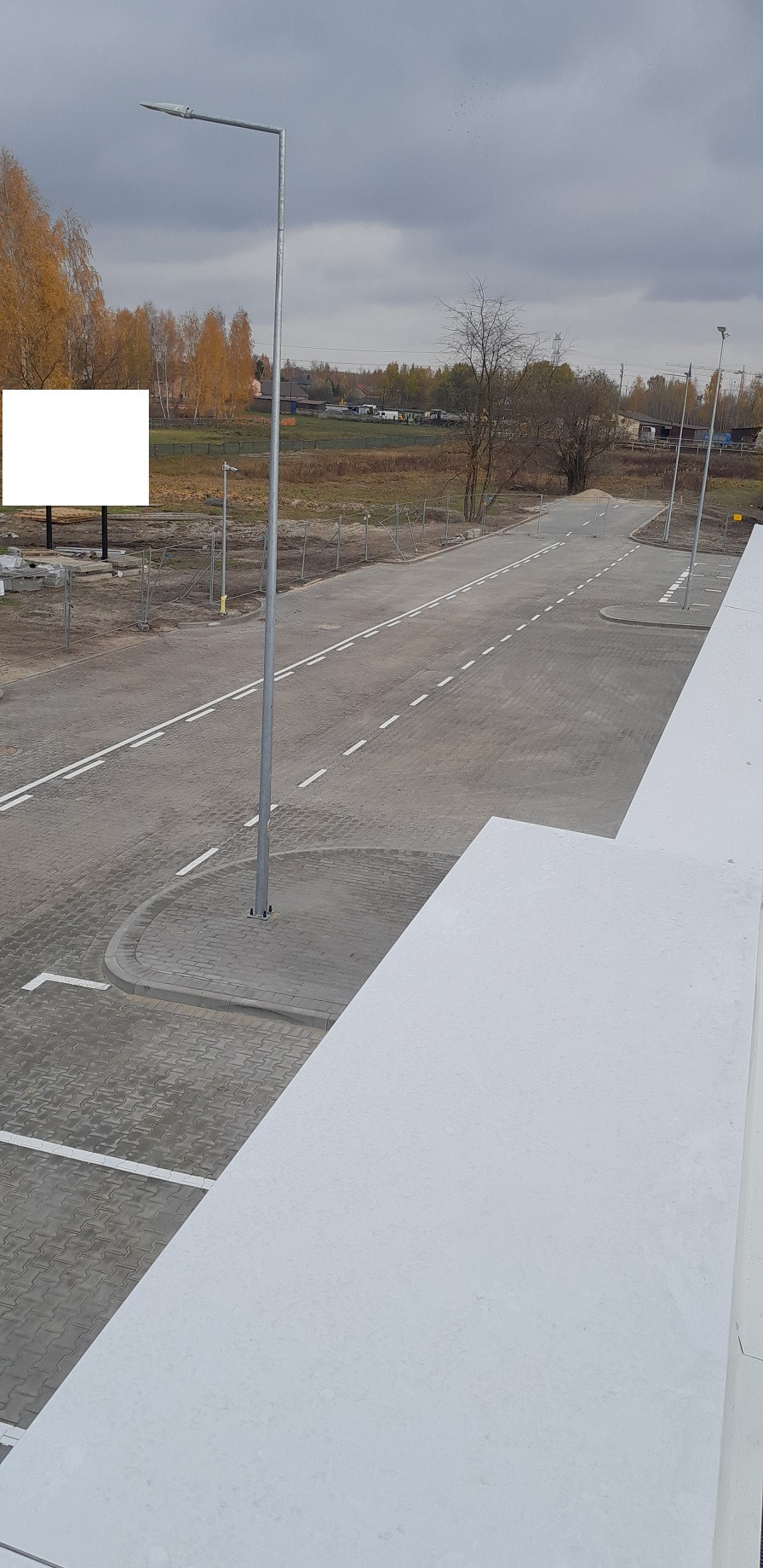 Nowa droga z kostki brukowej z wyznaczonymi miejscami parkingowymi i oświetleniem ulicznym, widok z góry na tle jesiennego krajobrazu.