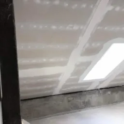 Płyty gipsowo-kartonowe na poddaszu z widocznymi łączeniami i otworem na okno dachowe przed szpachlowaniem, surowa ściana boczna.