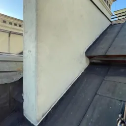 Szczegółowe ujęcie dachu z blachy z kominem przylegającym do ściany budynku, widoczne łączenia blachy i uszczelnienia.