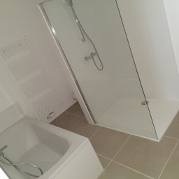 K&K BROTHERS RENOVATION - Jasna łazienka po remoncie: kabina prysznicowa ze szklanymi drzwiami, biała wanna z chromowaną armaturą, grzejnik drabinkowy i beżowe płytki podłogowe.