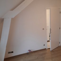 K&K BROTHERS RENOVATION - Pokój na poddaszu w trakcie malowania: białe ściany, drewniana podłoga, otwarte drzwi do sąsiedniego pomieszczenia z widocznym zabezpieczeniem podłogi.