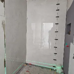 Łazienka w trakcie remontu: częściowo wyłożone płytki, poziomica laserowa wyznacza linie, widoczne narzędzia glazurnicze i akcesoria montażowe.