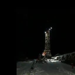 Oświetlona wieża wiertnicza w zimowej scenerii, nocne ujęcie z pracownikami w odblaskowych kamizelkach, śnieg na ziemi i rury wiertnicze w pobliżu