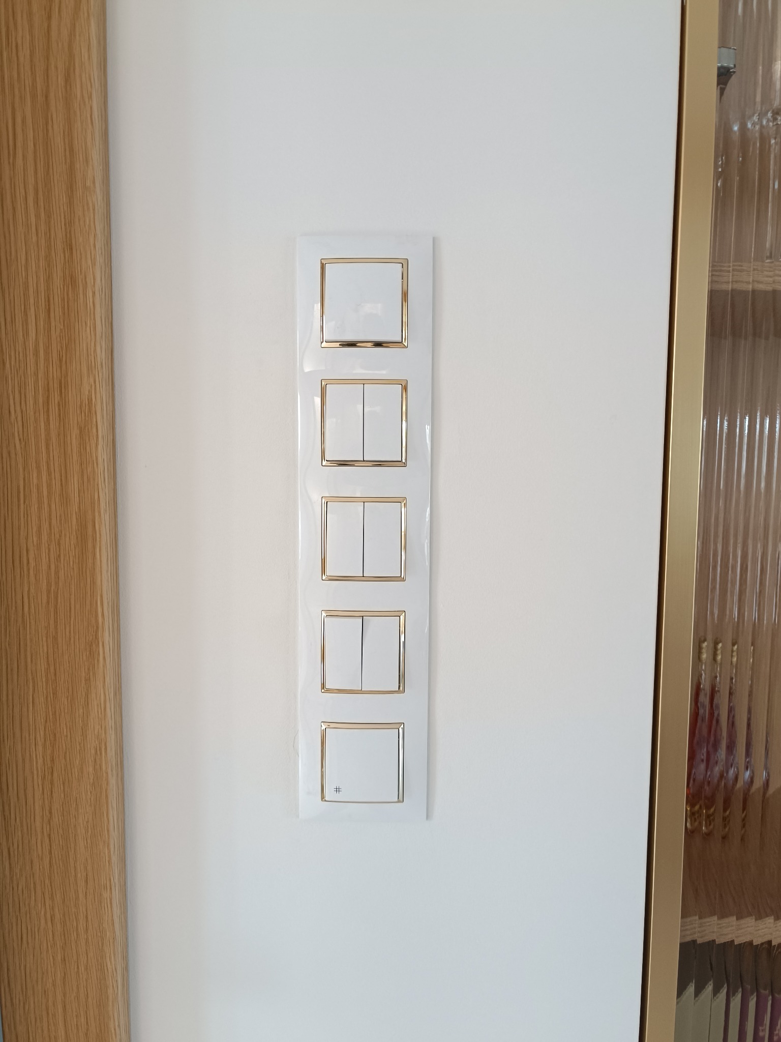 Panel z pięcioma białymi włącznikami światła z delikatnym złotym obramowaniem zamontowany na białej ścianie, widok z bliska.