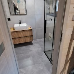 May bud - Wykończona łazienka w stylu skandynawskim: szare płytki, drewniana szafka pod umywalką, kabina prysznicowa z czarnymi ramami. Widoczne narzędzia na podłodze.