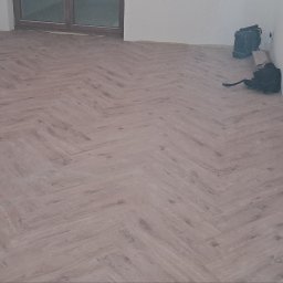 May bud - Ukończona podłoga z paneli ułożonych w jodełkę, widoczne gniazdka elektryczne i okno. Na parapecie puszka napoju energetycznego.