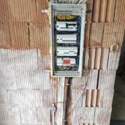 Rozdzielnica elektryczna zamontowana na ścianie z cegieł ceramicznych, widoczne kable i przewody w peszlach, instalacja w trakcie montażu.
