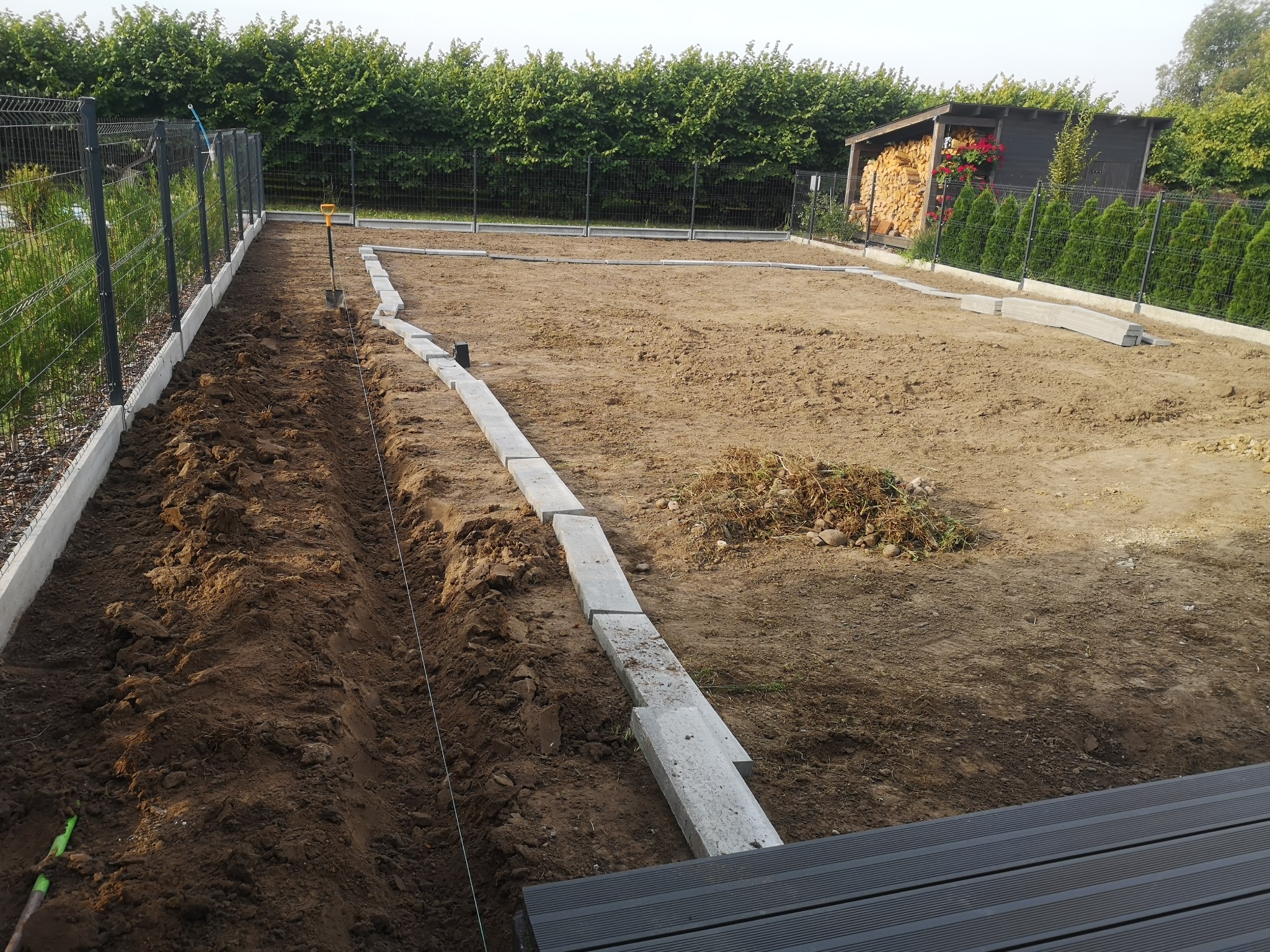 Przygotowanie terenu pod budowę obrzeży trawnika: wykopany rów, ułożone betonowe krawężniki, widoczna szpadel i rozciągnięty sznurek.