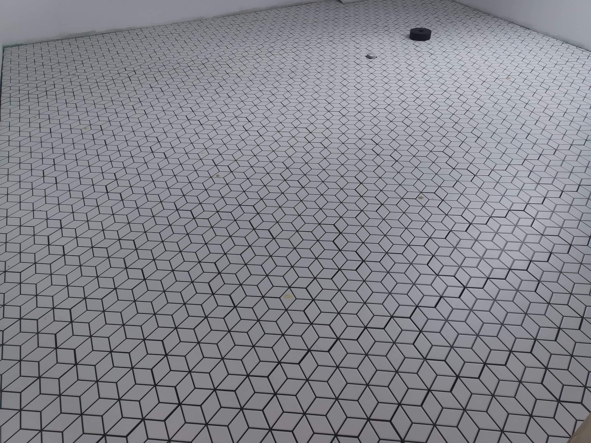 Ukończona podłoga w łazience wyłożona białymi, sześciennymi płytkami z czarnym obrysem, widoczny odpływ liniowy.