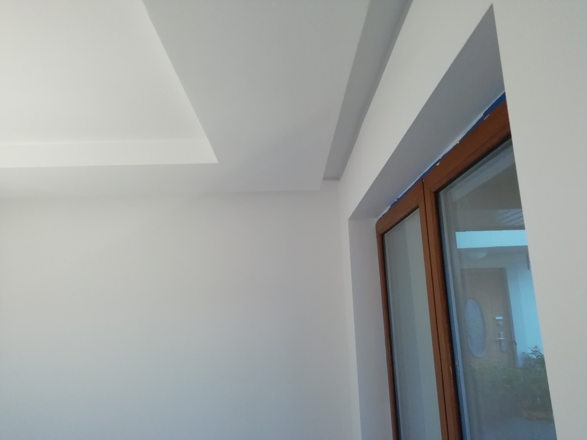 Świeżo pomalowane na biało wnętrze z widocznym oknem w drewnianej ramie i dekoracyjnym podwieszanym sufitem.