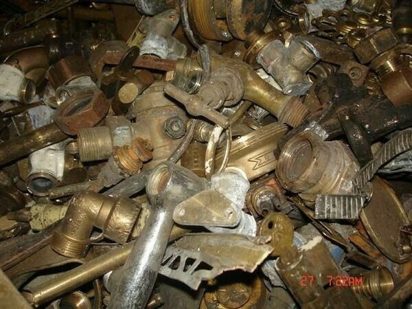 Stos zdemontowanych, mosiężnych zaworów i złączek hydraulicznych, widoczne ślady korozji i osadów.