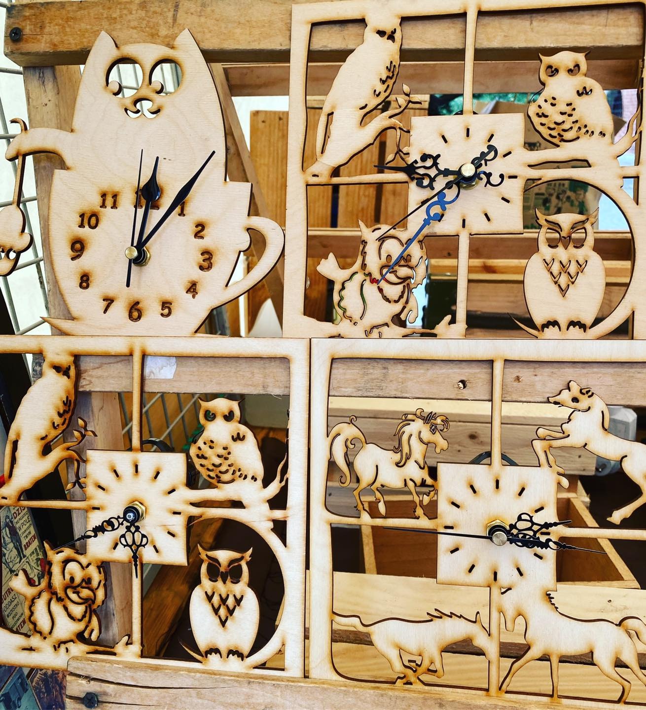 Ręcznie robione, drewniane zegary z motywami zwierzęcymi: kot w filiżance, sowy i konie, każdy umieszczony w kwadratowej ramce.