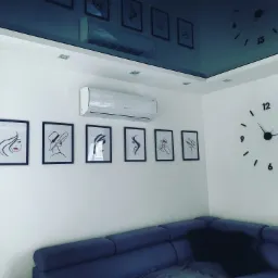 Biała klimatyzacja ścienna zamontowana w nowoczesnym salonie z dekoracyjnymi obrazami i dużym zegarem na ścianie.