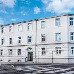 Trzypiętrowy budynek biurowy z białymi ścianami i licznymi oknami, widoczny z perspektywy ulicy z przejściem dla pieszych.