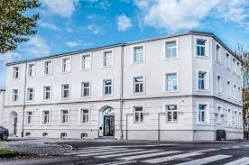 Trzypiętrowy budynek biurowy z białymi ścianami i licznymi oknami, widoczny z perspektywy ulicy z przejściem dla pieszych.