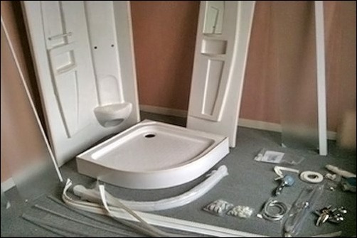 Nierozpakowana kabina prysznicowa z brodzikiem i panelem, elementy montażowe leżą na podłodze, widoczne instrukcje w foliowych opakowaniach.