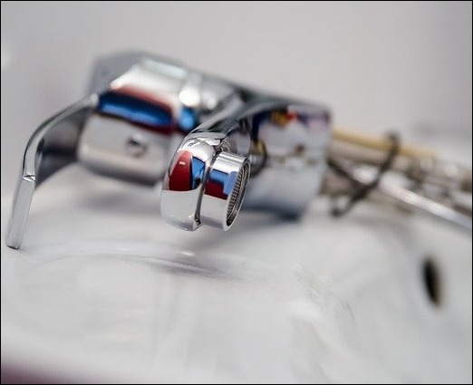 Błyszcząca, chromowana bateria umywalkowa z widocznymi odbiciami, zamontowana na białej umywalce, z narzędziami w tle, ukazująca detale instalacji.