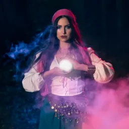 Kobieta w kostiumie wróżki trzymająca świecącą kulę w dłoniach, otoczona niebieskim i różowym dymem na tle ciemnego lasu.