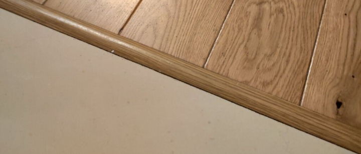 Połączenie jasnej podłogi drewnianej z kremową powierzchnią, wykończone listwą przypodłogową o barwie zbliżonej do drewna.