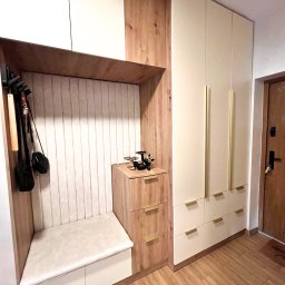 Michał Lodarski - Funkcjonalna zabudowa przedpokoju z siedziskiem, wieszakami i szafą z jasnymi frontami i złotymi uchwytami. Drewnopodobne wykończenie dodaje ciepła.