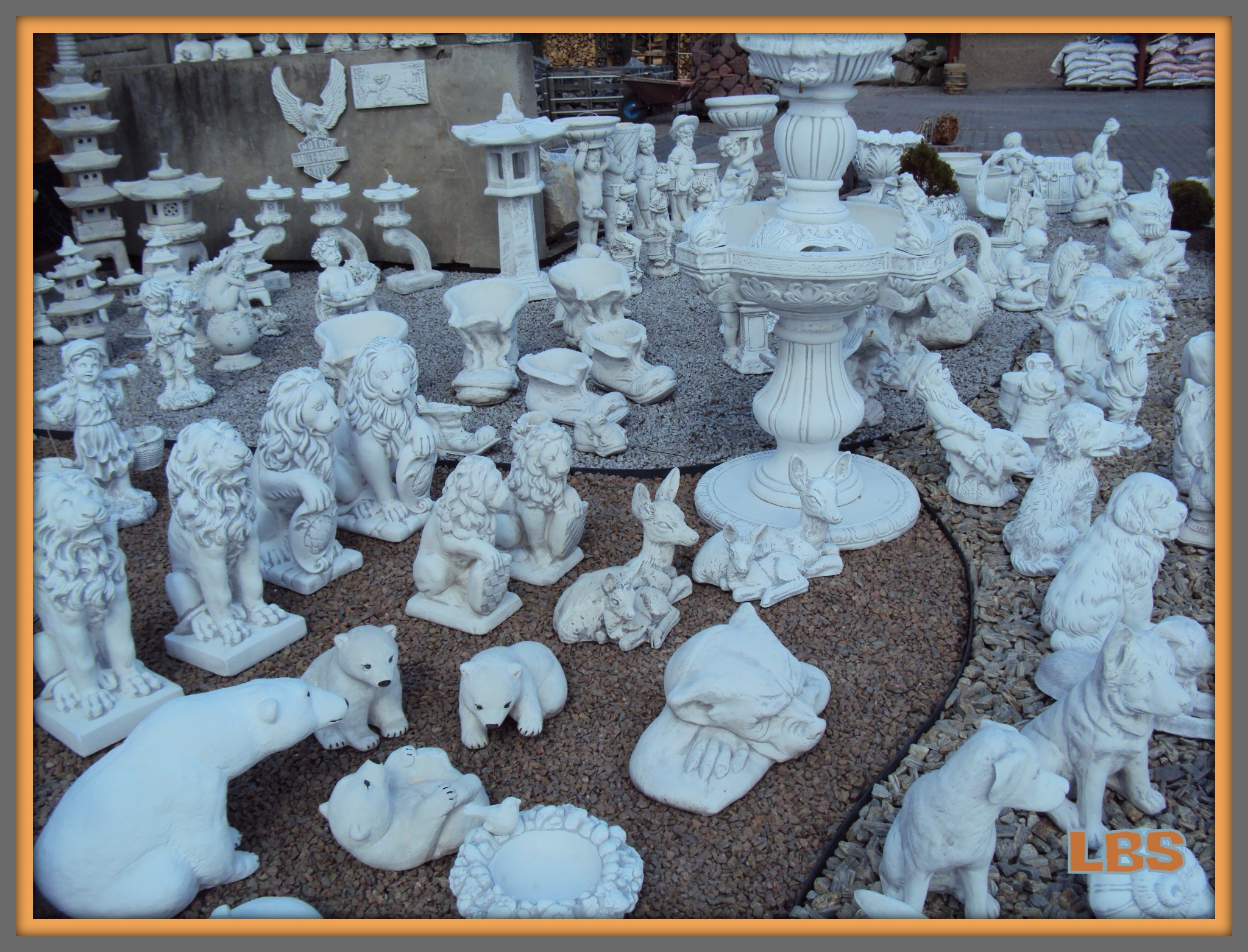 Ekspozycja różnych, białych, betonowych figur ogrodowych: zwierząt (lwy, niedźwiedzie, psy, jelenie), postaci, fontanny i lampionów na żwirowym podłożu.