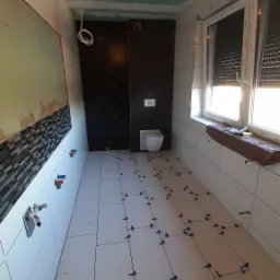 Łazienka w trakcie prac: białe płytki podłogowe z krzyżykami dystansowymi, częściowo ułożona mozaika na ścianie, czarne panele ścienne, sufit z płyt kartonowo-gipsowych przed szpachlowaniem.