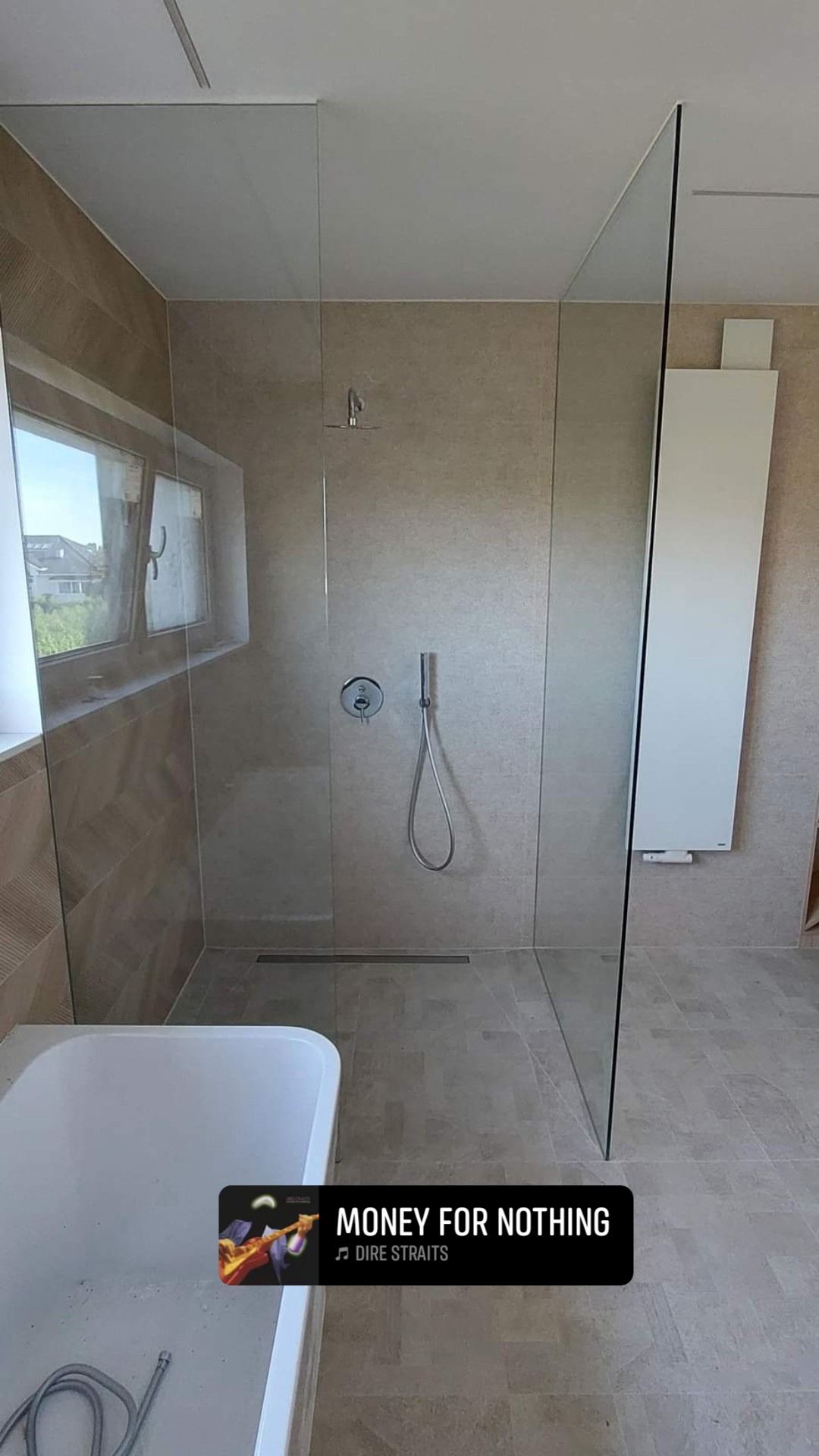 Nowoczesna kabina prysznicowa typu walk-in z transparentnego szkła, zamontowana w łazience wykończonej beżowymi płytkami; widoczny odpływ liniowy, bateria podtynkowa i grzejnik drabinkowy.