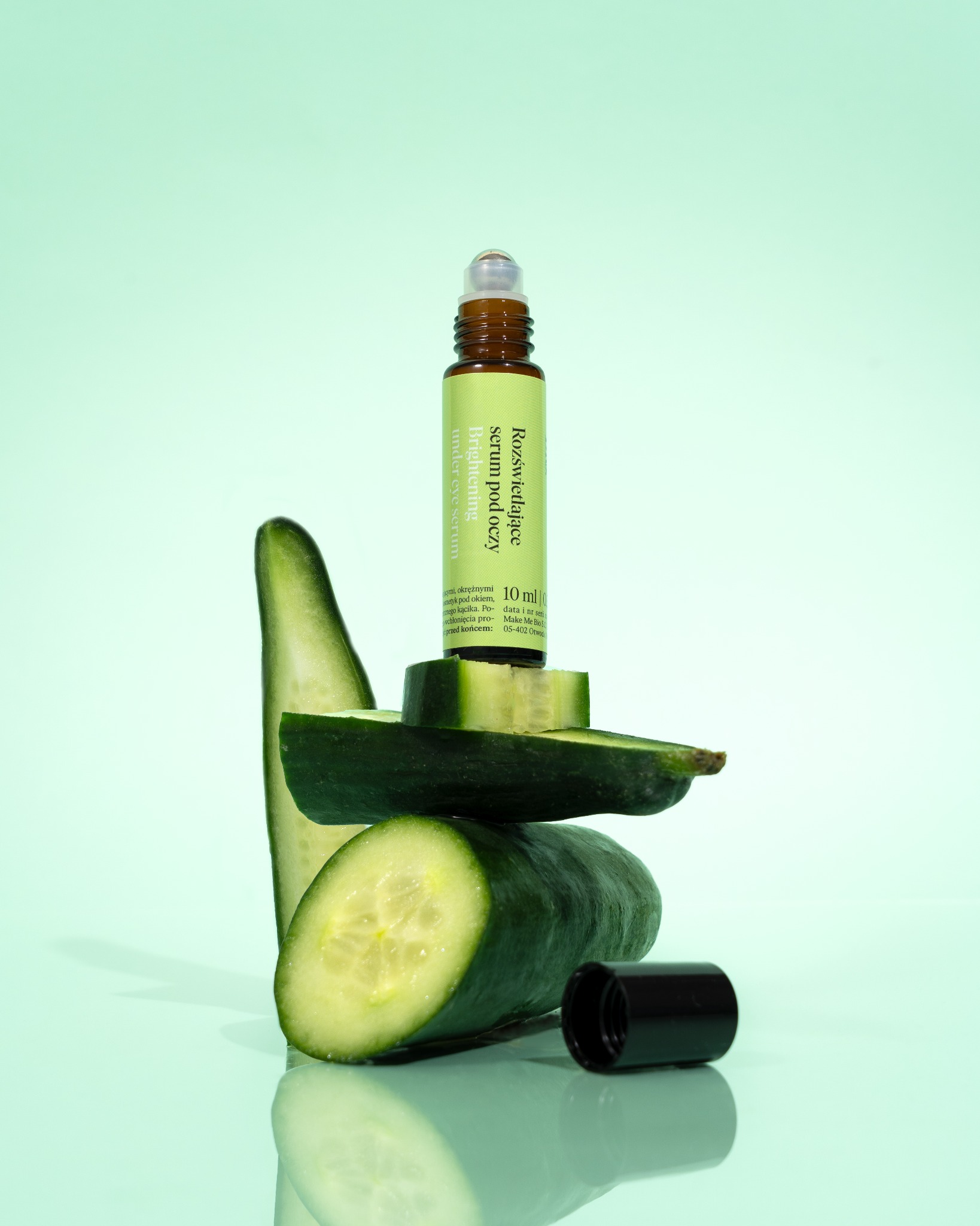 Serum pod oczy na piramidzie z ogórków na tle miętowym. Fotografia produktowa podkreśla naturalny skład i świeżość produktu.