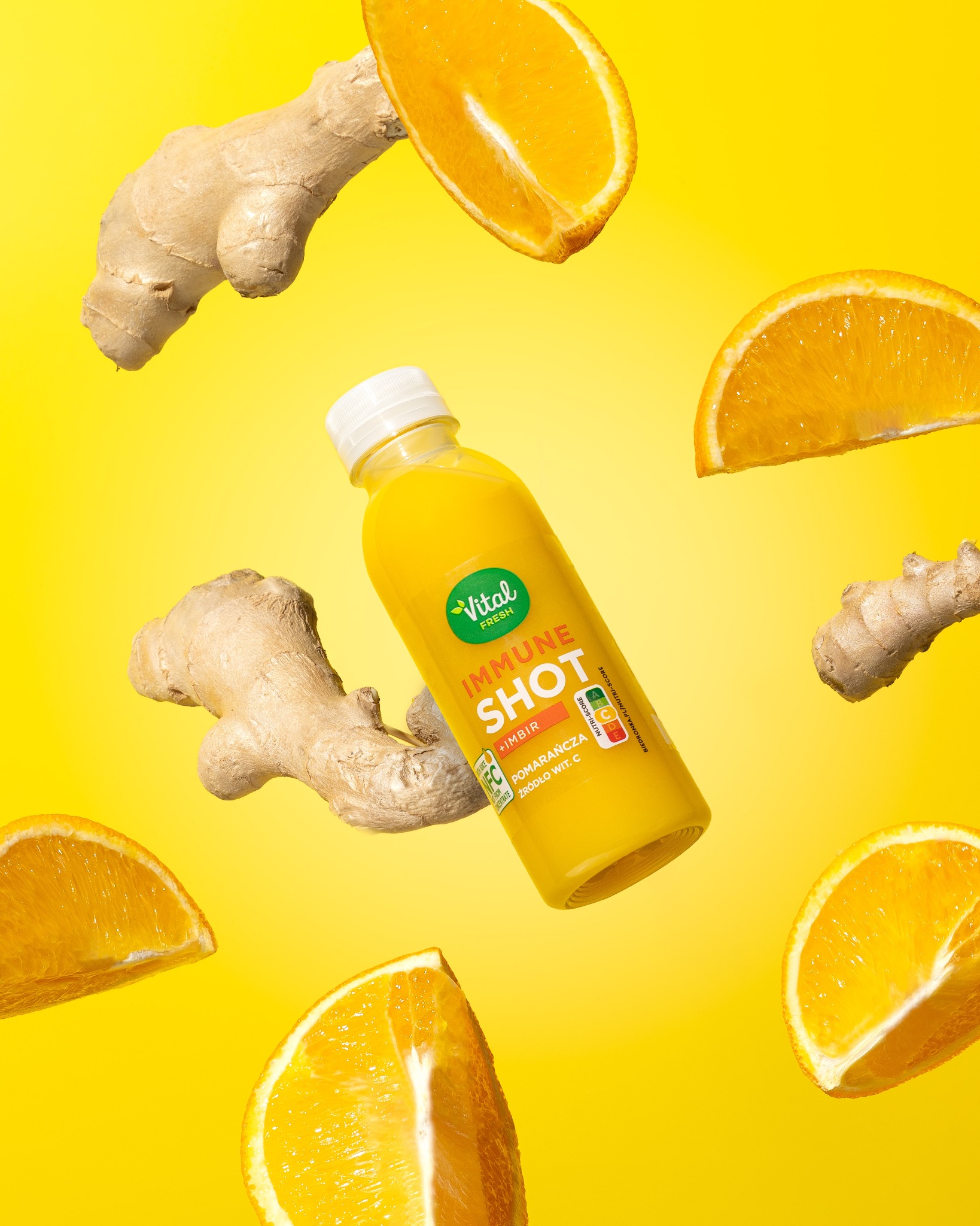 Zdjęcie produktowe: butelka soku Vital Fresh Immune Shot z imbirem i pomarańczą, otoczona plastrami pomarańczy i korzeniami imbiru na żółtym tle.