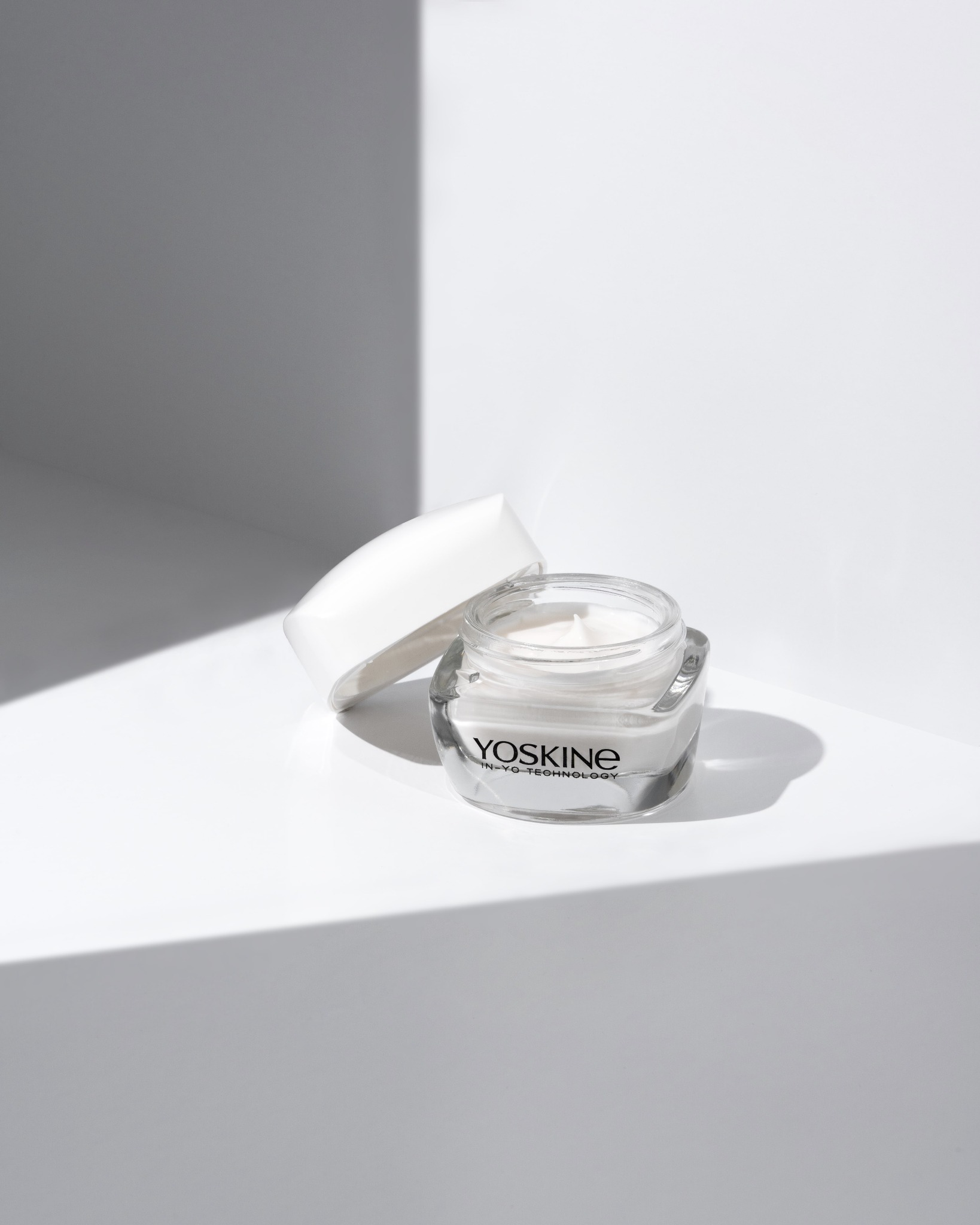 Minimalistyczne ujęcie słoiczka kremu Yoskine na białym tle z cieniem, z otwartym wieczkiem, prezentujące produkt w czystym, nowoczesnym stylu.