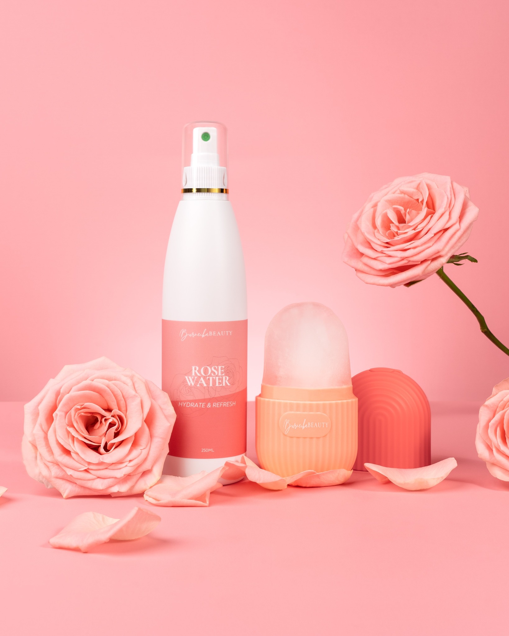 Różowa fotografia produktowa: woda różana w sprayu, roller do twarzy i maska silikonowa, otoczone różami i płatkami na jednolitym tle.