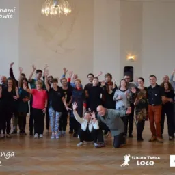 Grupowe zdjęcie uczestników warsztatów tanga w Chrzanowie, luty 2022, z podniesionymi rękami, z logo szkoły tańca Loco i informacjami kontaktowymi w rogu.
