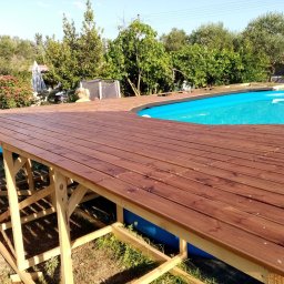 MARKTECH MAREK SZPRÓCH - Nowy, drewniany taras z brązowych desek wokół basenu ogrodowego, konstrukcja z jasnego drewna, widok na zieleń ogrodu i błękit nieba.