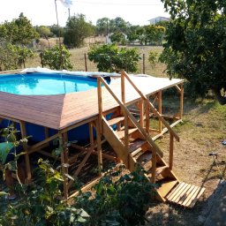 MARKTECH MAREK SZPRÓCH - Ogród z naziemnym basenem, drewnianym podestem i schodami w trakcie budowy, widoczne elementy konstrukcyjne i osoba pracująca przy wykończeniu.