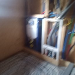 MARKTECH MAREK SZPRÓCH - Niedokładne zdjęcie instalacji ogrzewania podłogowego z rozdzielaczem i rurami w trakcie montażu w pomieszczeniu wykończonym płytami drewnopodobnymi.