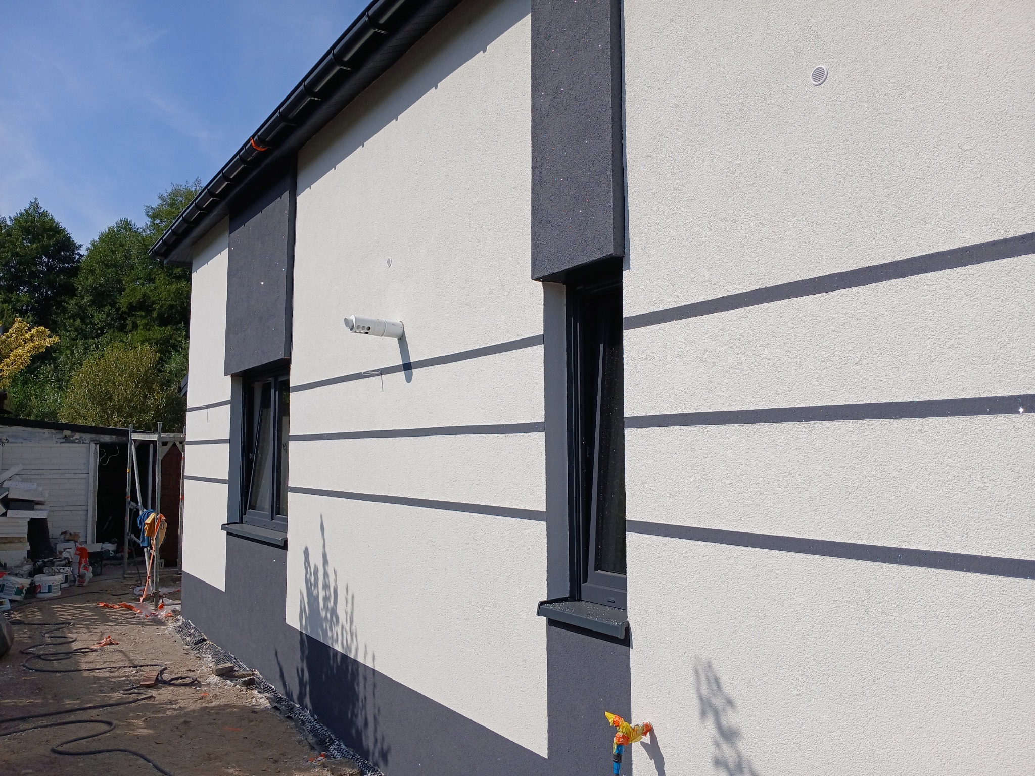 Nowoczesna elewacja domu w Częstochowie z szarymi akcentami i oknami. Widoczne rusztowania i materiały budowlane sugerują prace wykończeniowe.