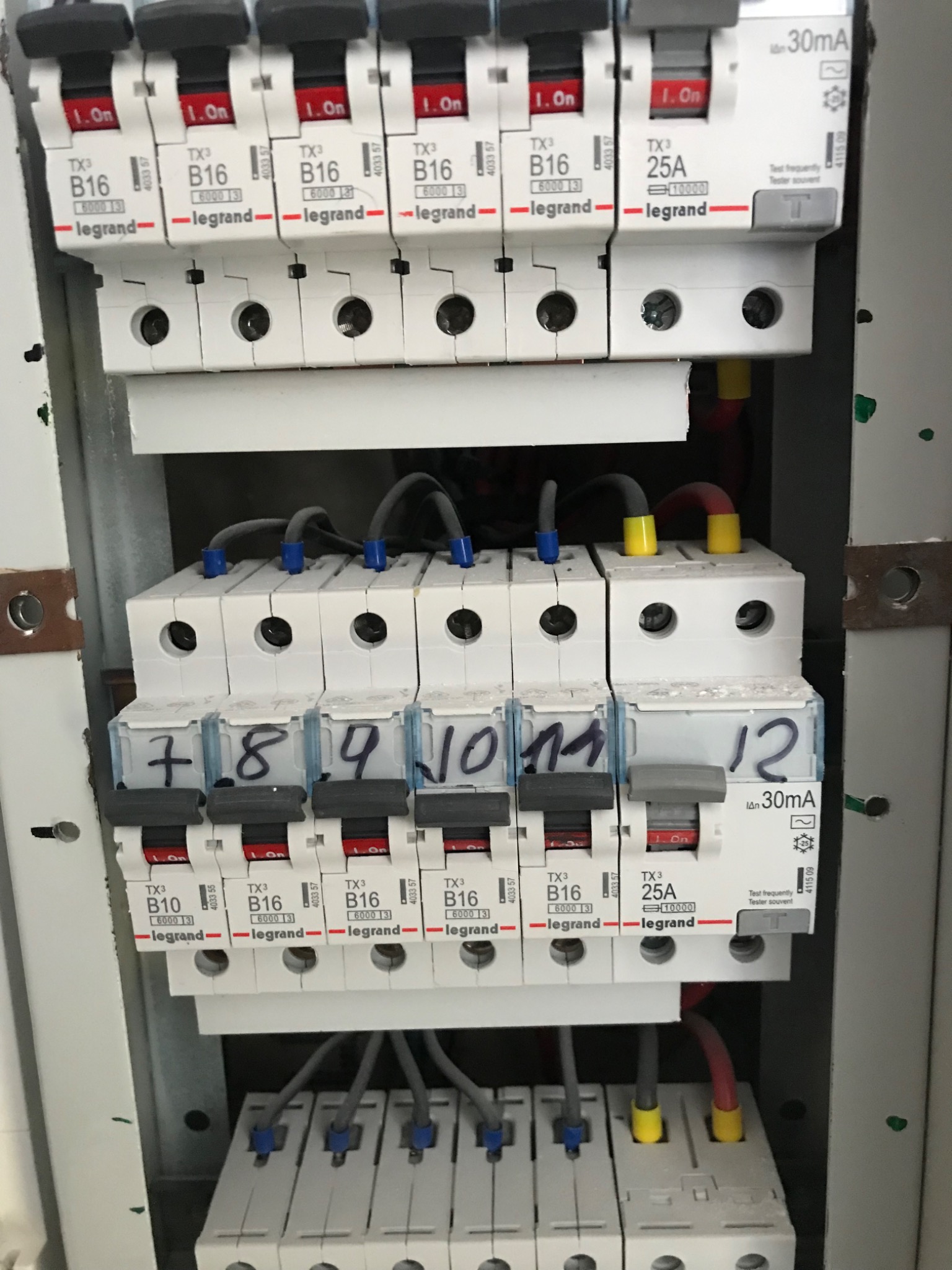 Rozdzielnica elektryczna z zainstalowanymi bezpiecznikami Legrand TX3 B16 i 25A, z numeracją od 7 do 12 naniesioną odręcznie na obudowach.