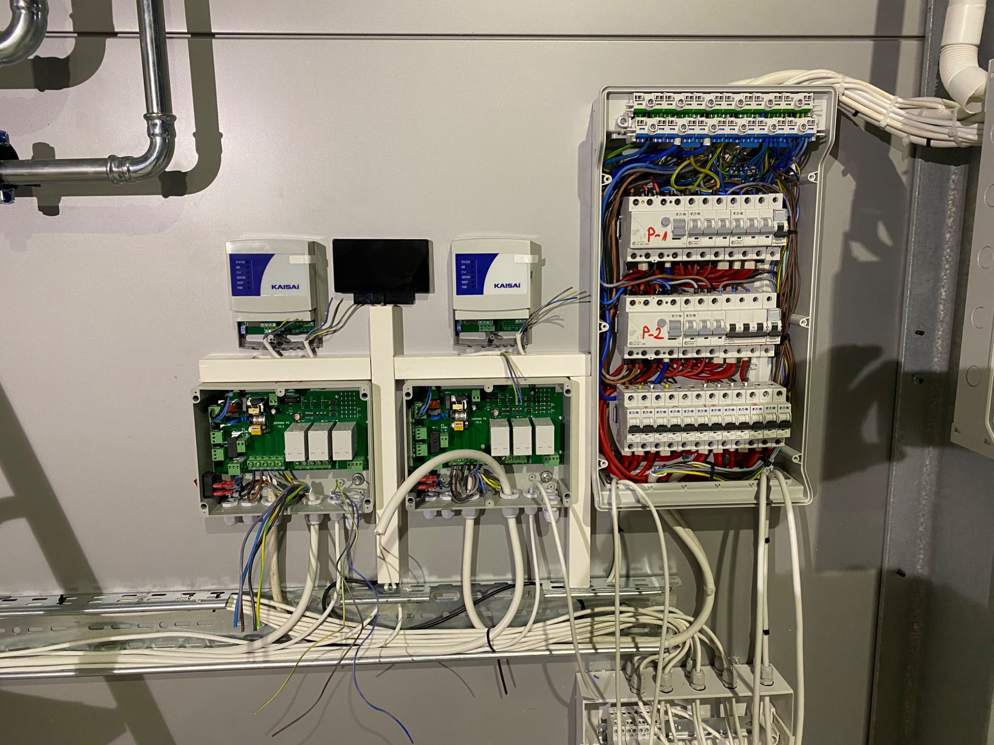 Rozdzielnica elektryczna z widocznymi bezpiecznikami, przewodami i modułami sterującymi Kaisai, zamontowana na szarej ścianie w pomieszczeniu technicznym.
