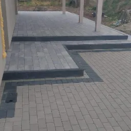 Nowo ułożona, szara kostka brukowa tworząca taras z zadaszeniem na drewnianych słupach. Widoczne czarne obramowania i schody z kostki.