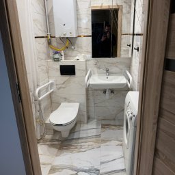KRISPOL Krystian Żuk - Wykończona łazienka z marmurowymi płytkami, umywalką z uchwytami dla niepełnosprawnych, toaletą, pralką i lustrem z odbiciem osoby robiącej zdjęcie.
