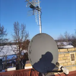 Antena satelitarna i antena kierunkowa na dachu budynku w Myślenicach, widoczne ślady użytkowania na antenie satelitarnej, błękitne niebo w tle.