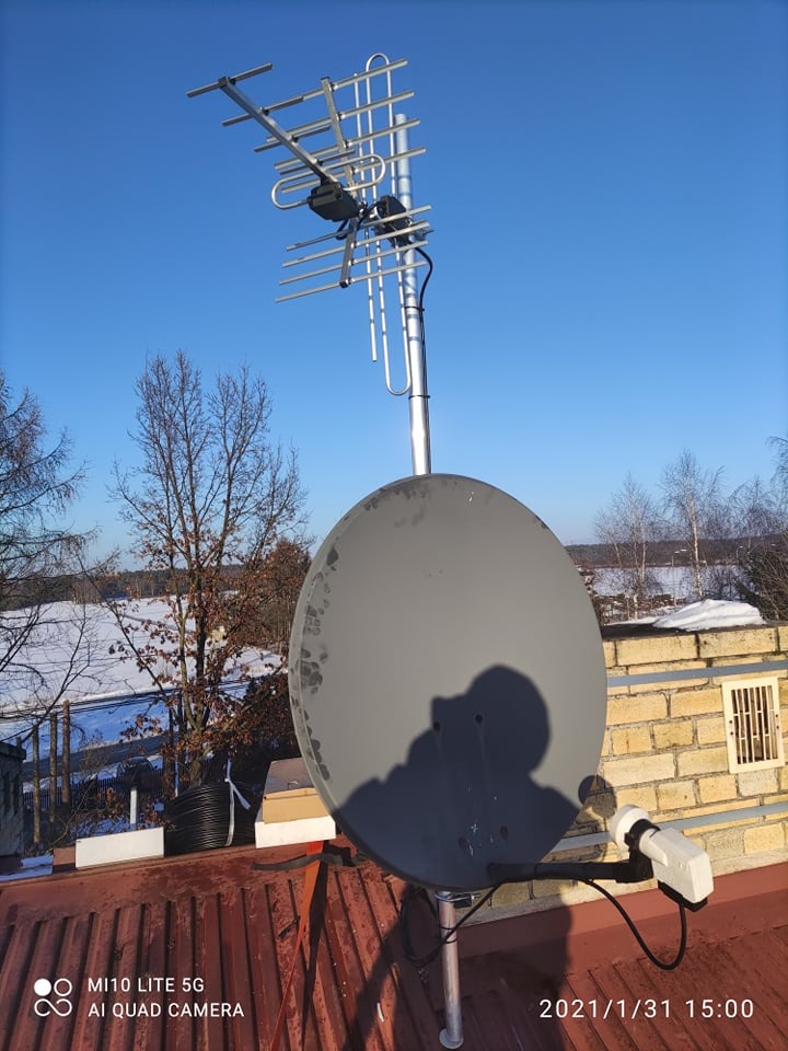 Antena satelitarna i antena kierunkowa na dachu budynku w Myślenicach, widoczne ślady użytkowania na antenie satelitarnej, błękitne niebo w tle.